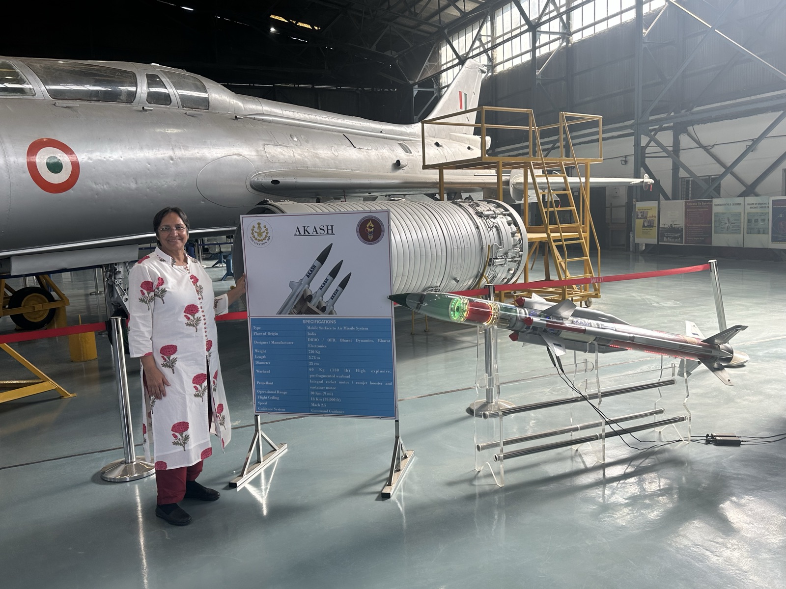Prameela beside an AKASH missile and fighter jet display from her DRDO years